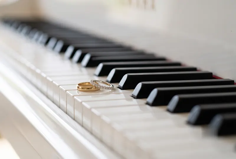 Two wedding rings resting on the keys of a white grand piano